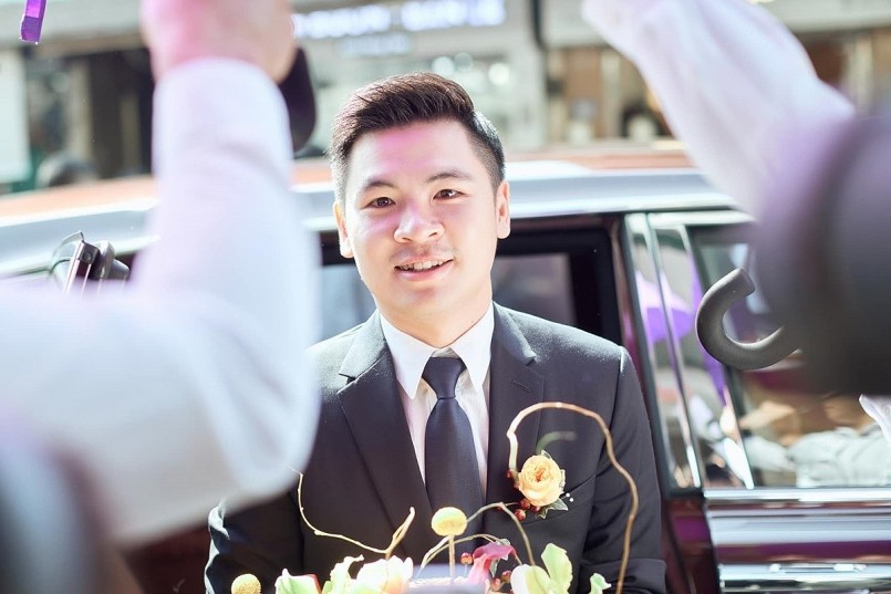 Đỗ Vinh Quang diện suit đen lịch lãm. Khi chú rể vừa bước vào cửa, đội ngũ bảo vệ có mặt sẵn, dùng dù tím che chắn để đảm bảo tính riêng tư của buổi lễ. An ninh được thắt chặt.